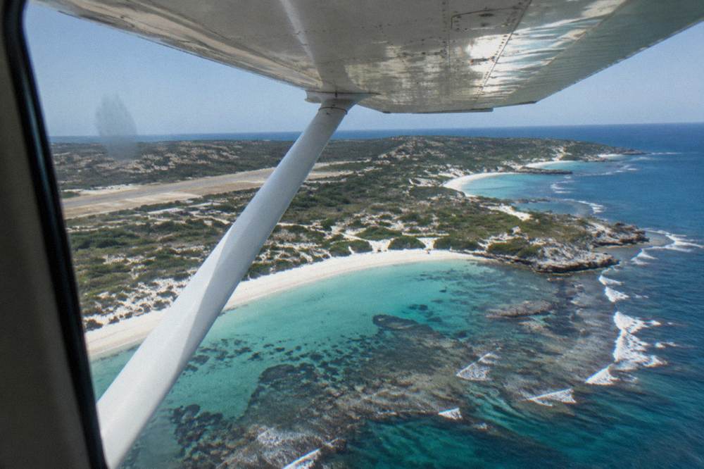 A light aircraft banking over an island coastline with white sand coves below