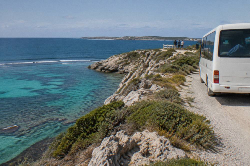 A tour bus pulled over at a coastal lookout with calm turquoise water and reef below
