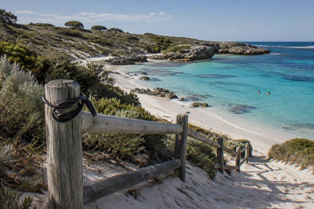A bicycle leaning on a wooden fence above a calm Rottnest bay with turquoise shallows