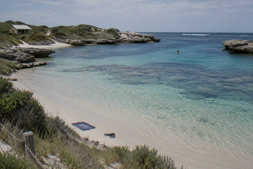 Clear shallow water and pale sand inside the reef bowl at The Basin, with bicycles parked near the beach