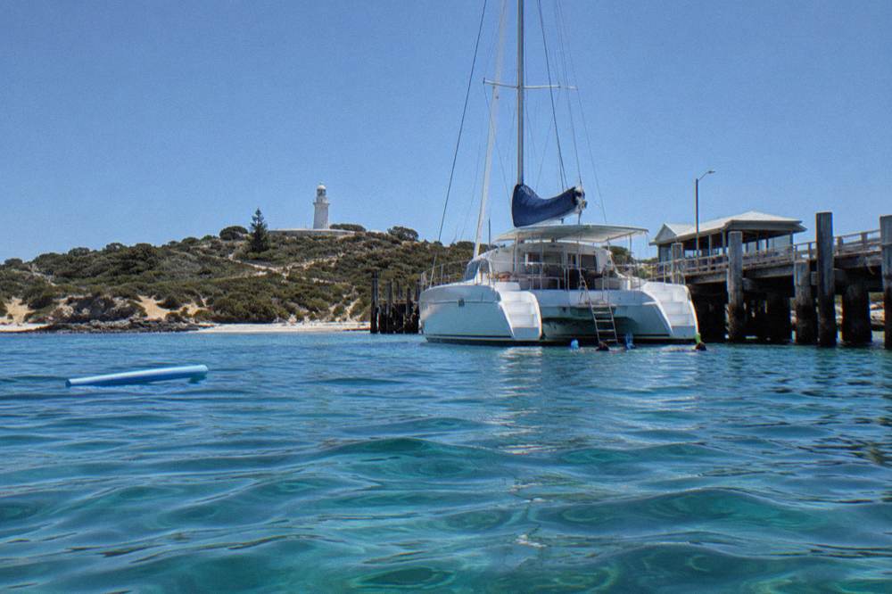 A catamaran anchored in a calm Rottnest bay with snorkellers in the water near the stern