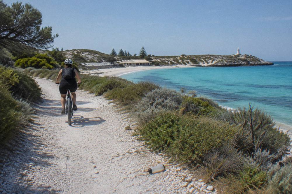 A cyclist riding a shared path beside turquoise water on Rottnest Island