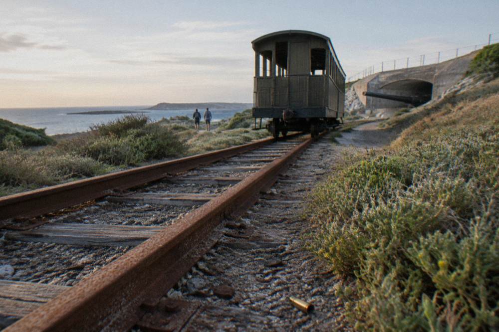 A heritage train carriage on a narrow track beside low coastal scrub on an island