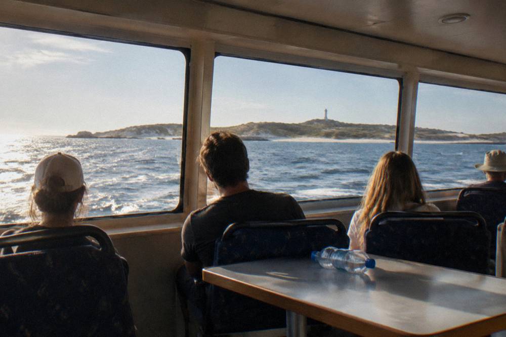 Passengers seated inside a ferry cabin looking out over open water towards an island