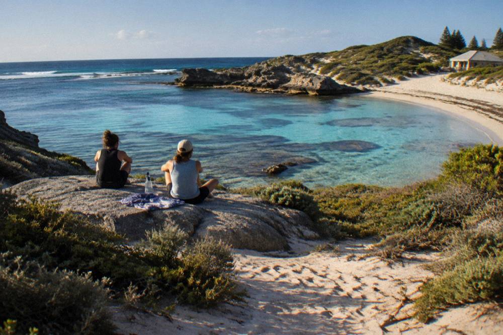 Cyclists resting beside a sandy path above a sheltered bay on Rottnest Island
