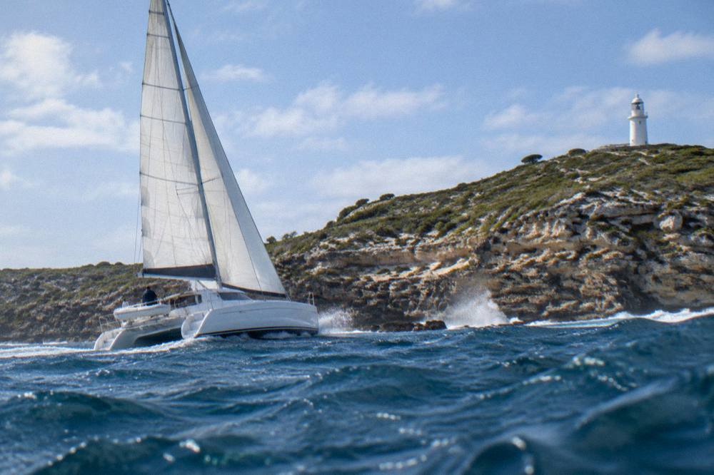 A catamaran under sail off a rocky headland at Rottnest Island