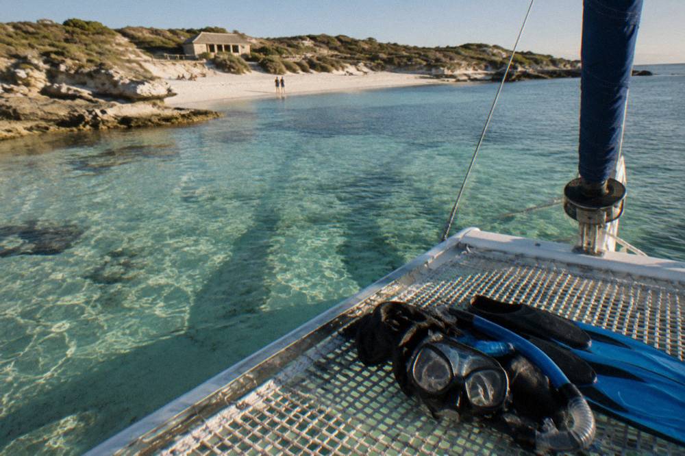 A sailing catamaran anchored over pale sand in clear shallow water at a Rottnest bay