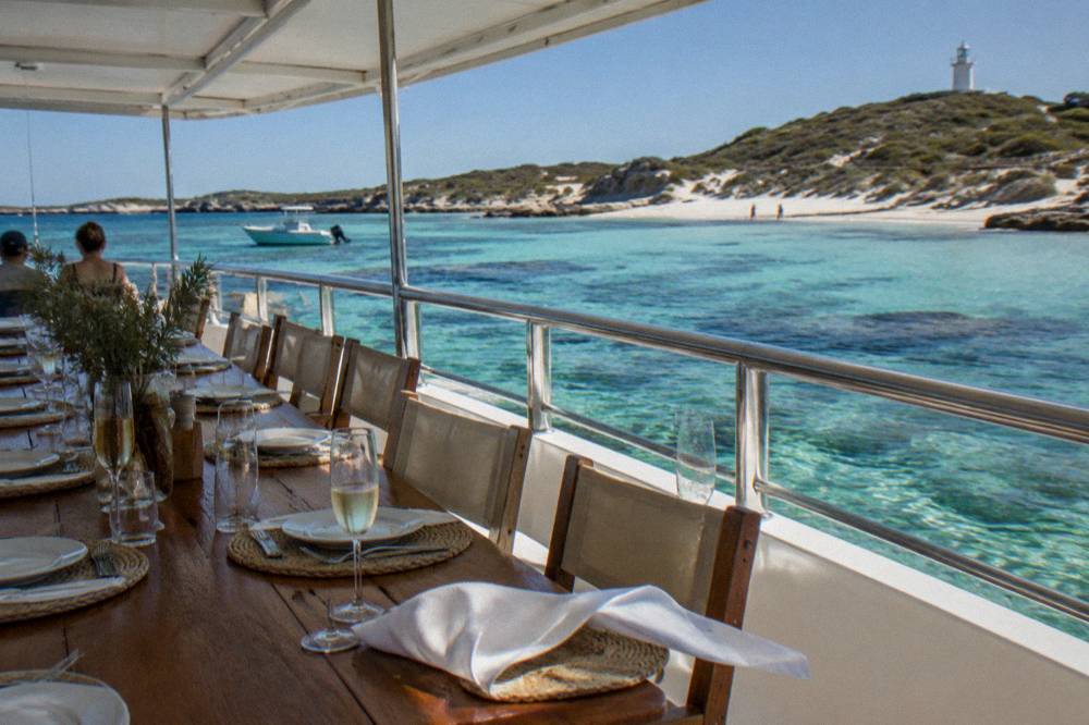A covered cruising boat at anchor in a sheltered bay with tables set on deck