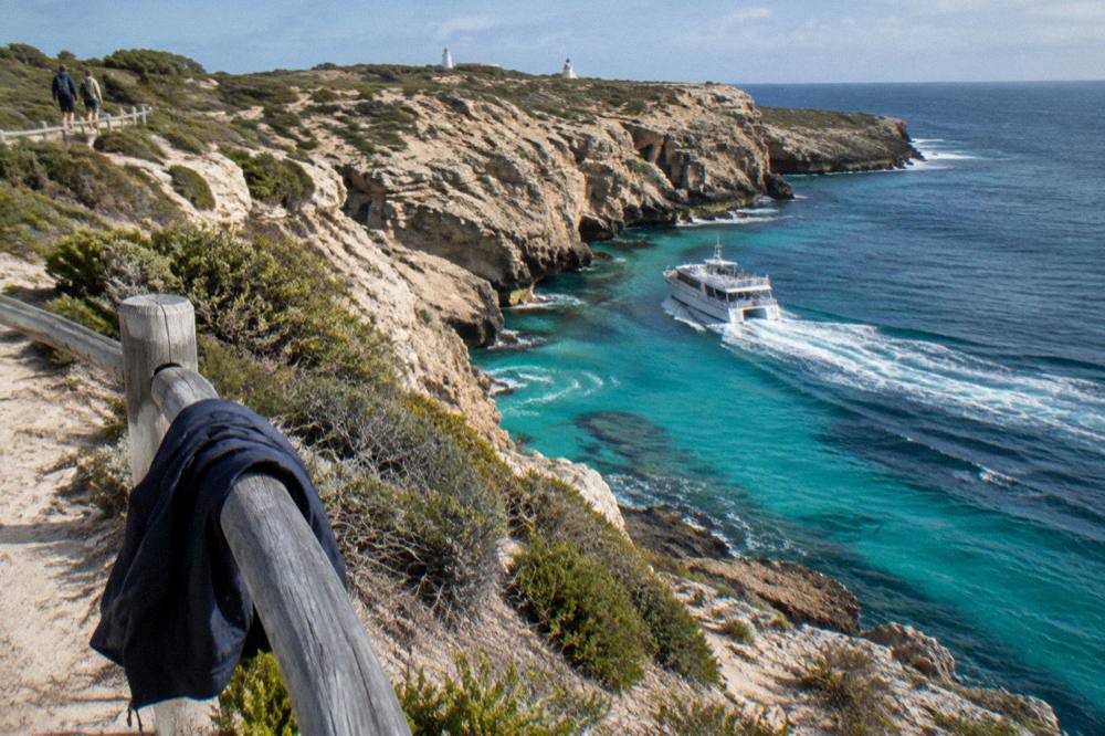 A small boat cruising past limestone cliffs and turquoise water on a Rottnest afternoon