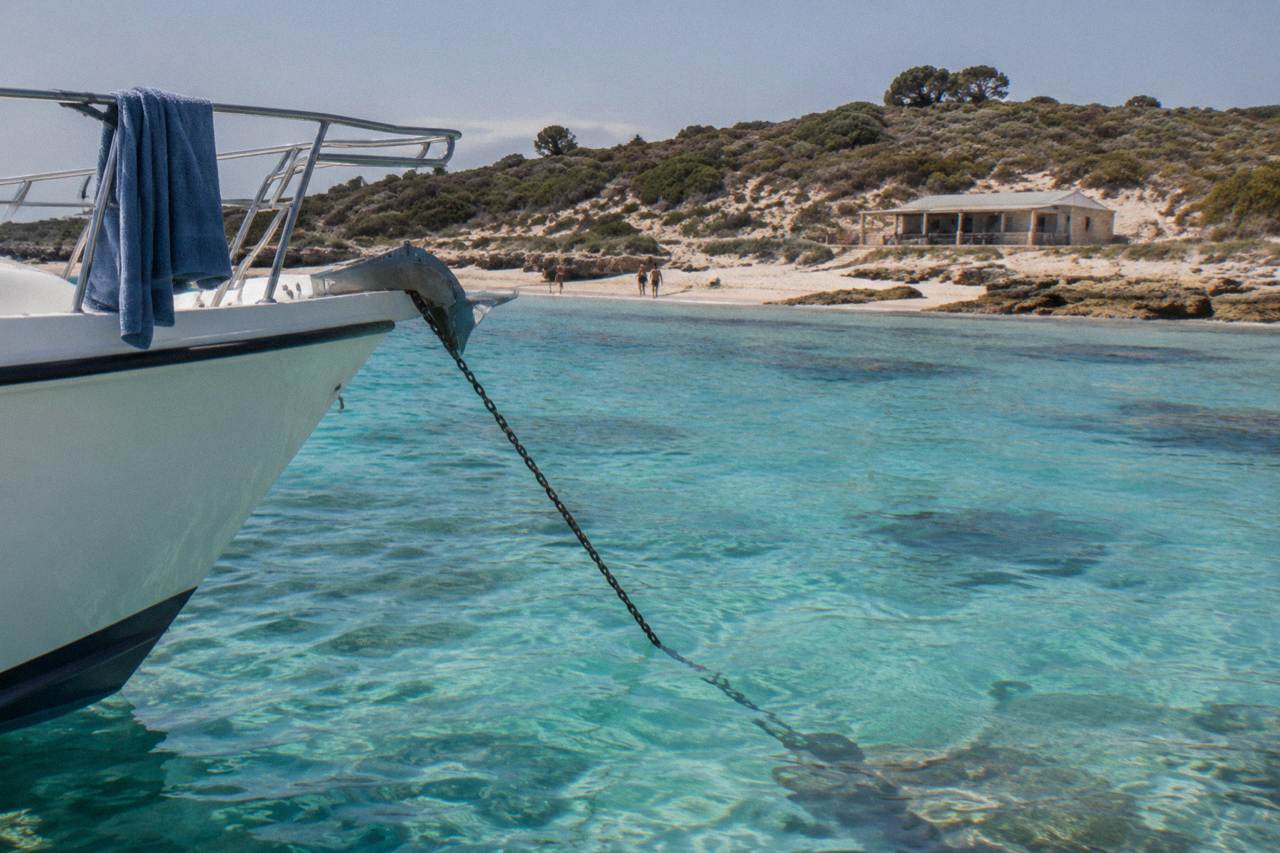 A charter boat moored in clear turquoise water beside a sandy Rottnest bay