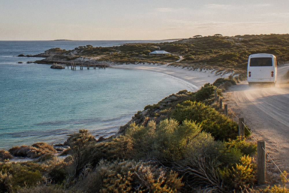 Island tour bus driving along a coastal road with turquoise bays on Rottnest Island