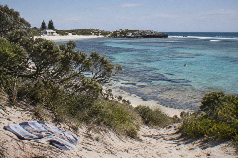 A cyclist riding a path above a sheltered bay with clear shallow water over reef