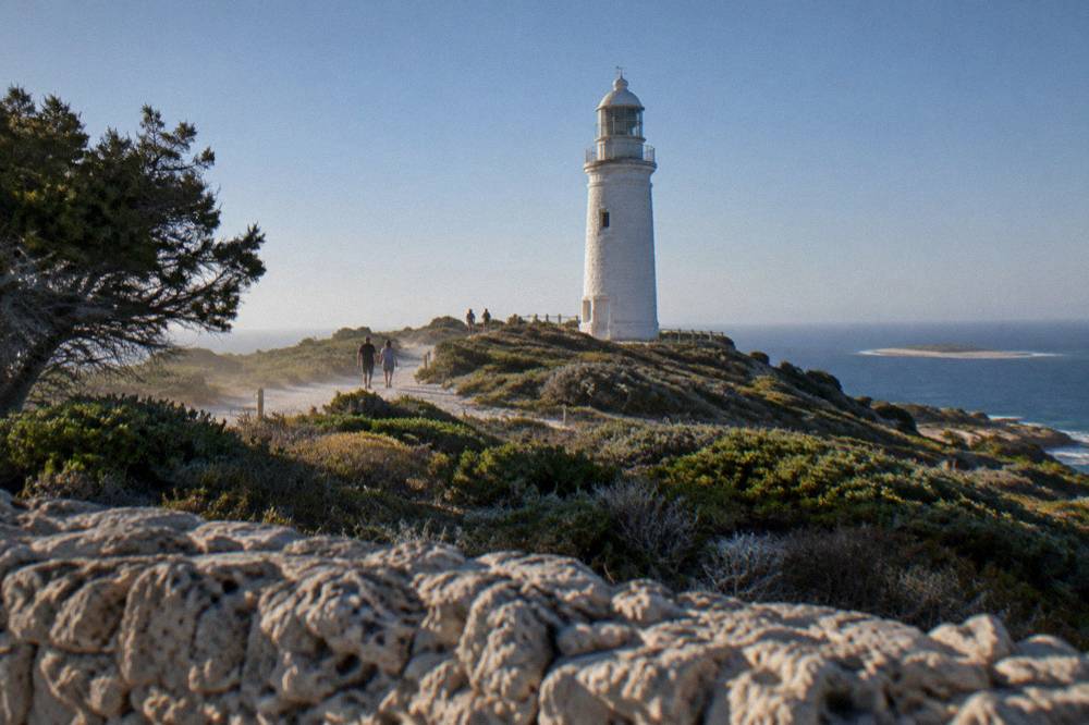 A white lighthouse above low coastal heath with the sea on the horizon