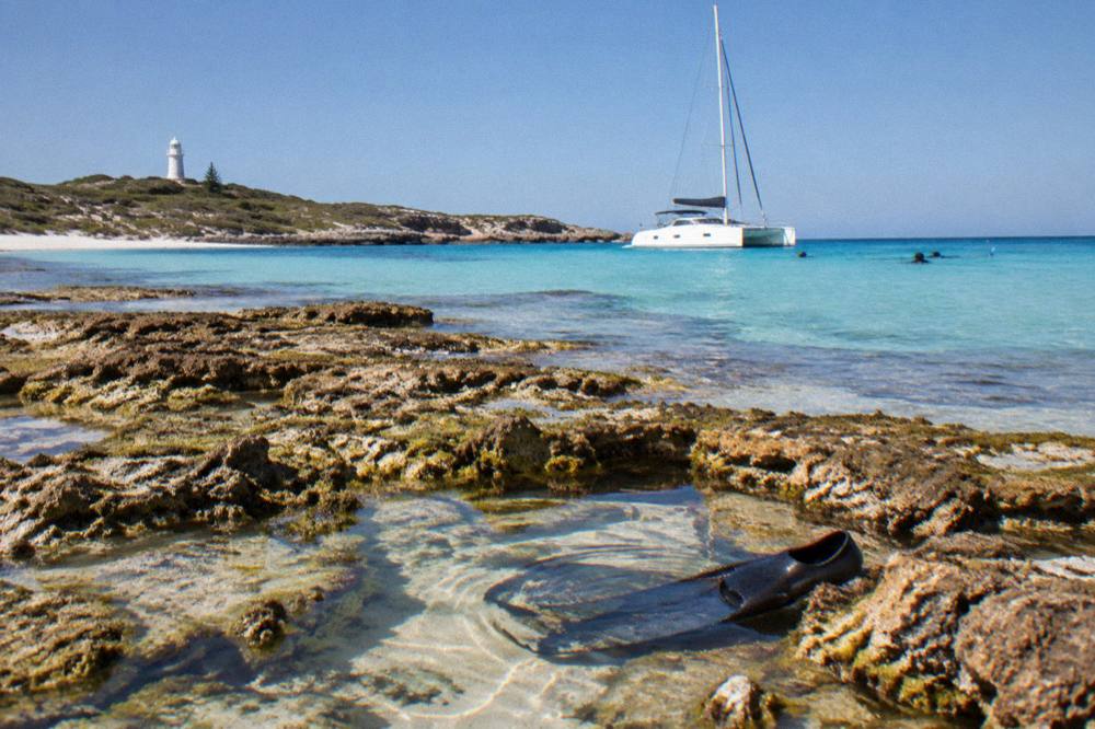 A catamaran anchored in a calm bay with snorkellers in the water near reef