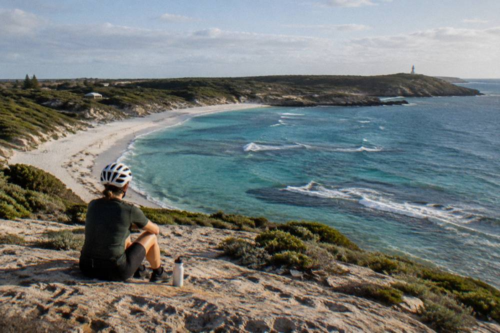 A cyclist resting beside a bike overlooking a quiet Rottnest bay
