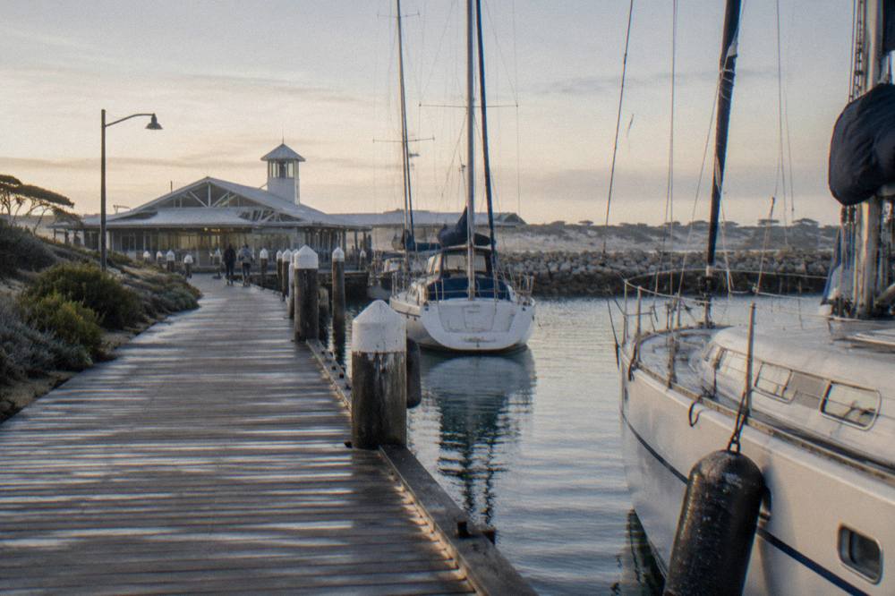 A sheltered marina at a boat harbour with moored yachts and a jetty in morning light