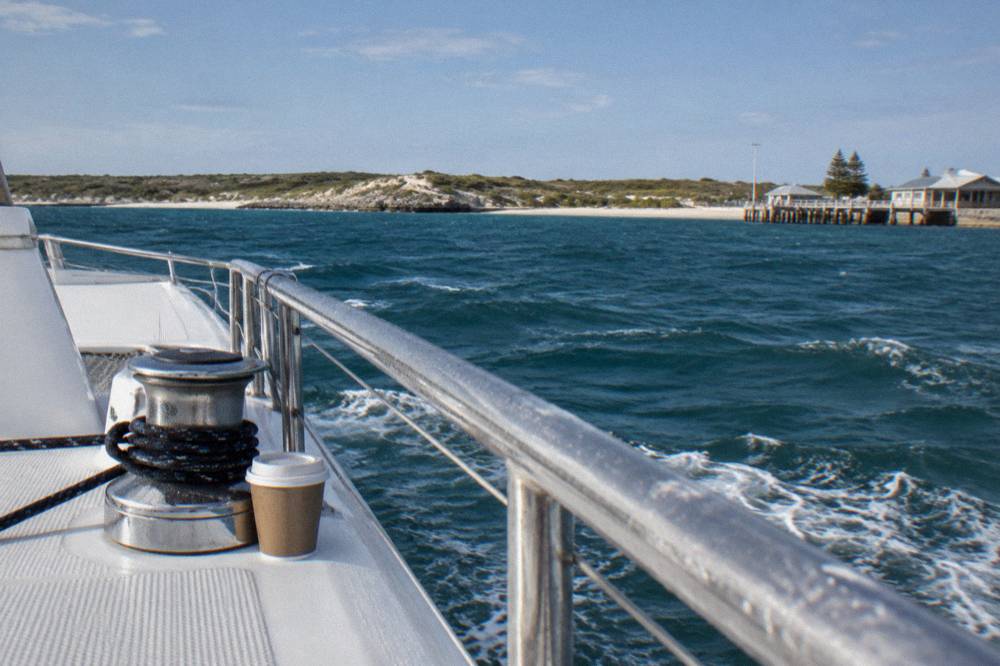 A passenger catamaran cutting across open blue ocean toward a low island on the horizon
