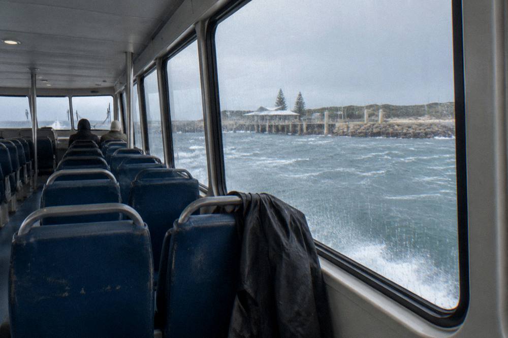 A ferry cabin interior with rows of seats and large windows looking out over open water