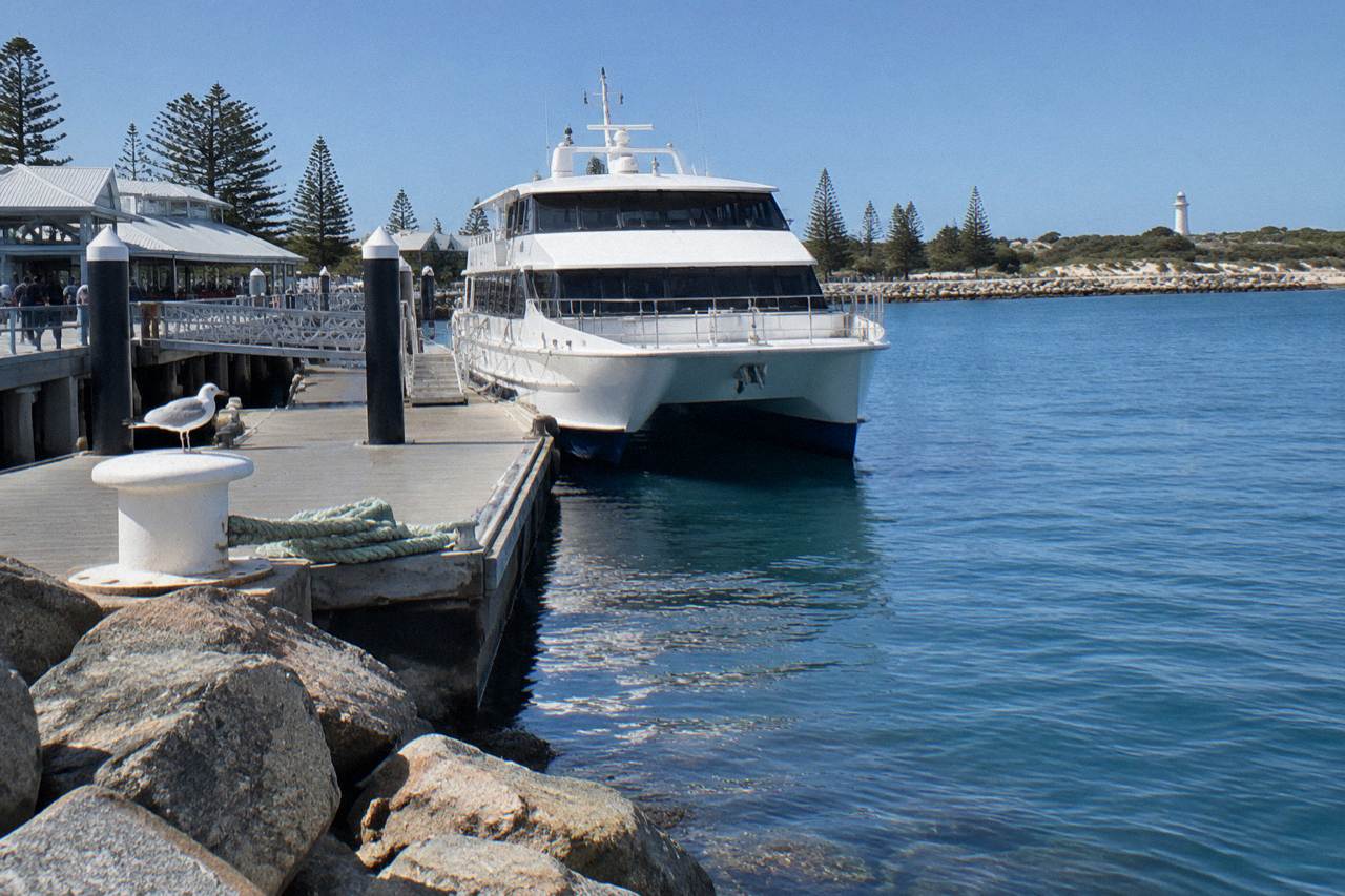 A passenger ferry moored at a marina jetty beside calm blue harbour water on a clear morning