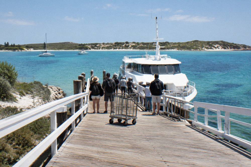 Ferry terminal jetty with passengers waiting beside a moored vessel under a clear sky