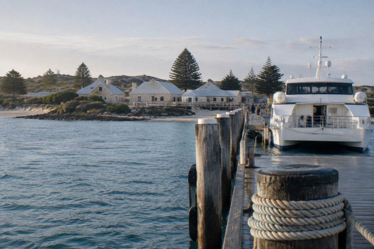 Ferry docked at a jetty on a calm morning with clear water and coastal buildings behind it
