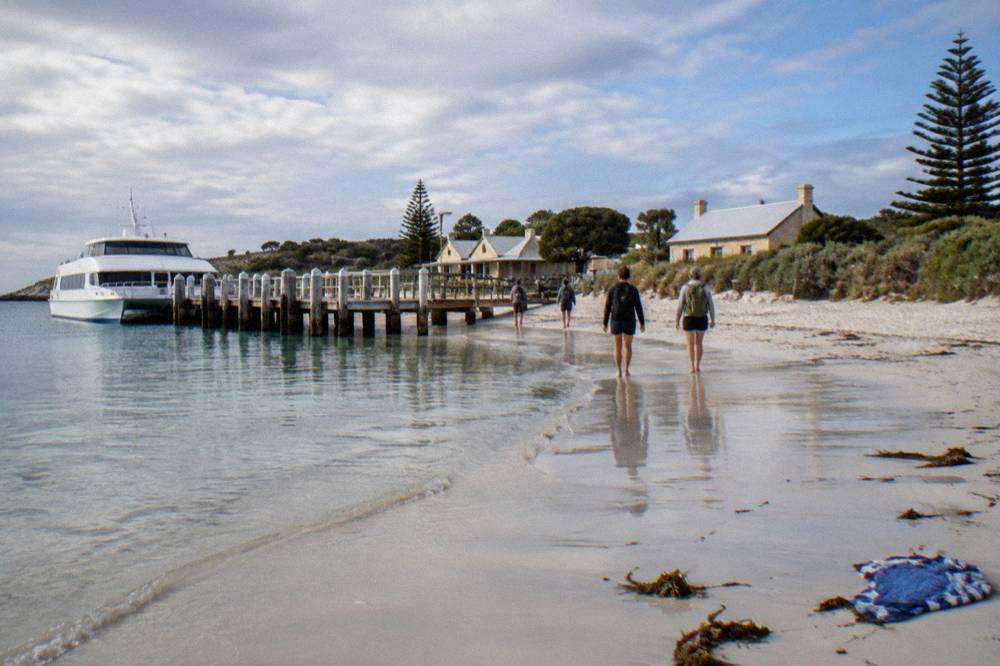 A ferry moored at a timber jetty with passengers walking toward a settlement of low buildings