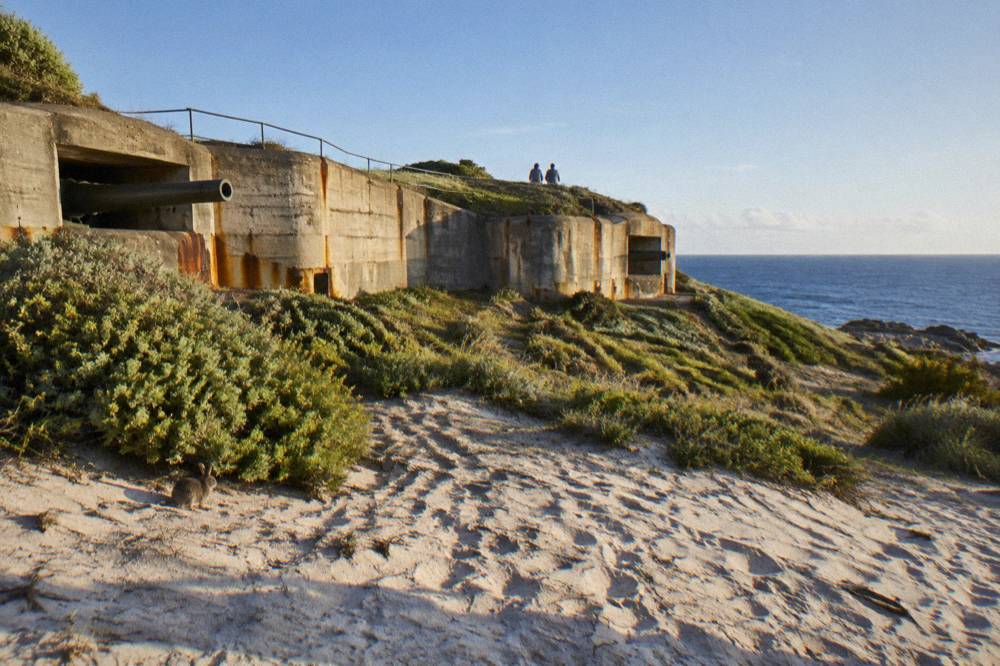 A stone military battery structure on a grassy hilltop above the sea
