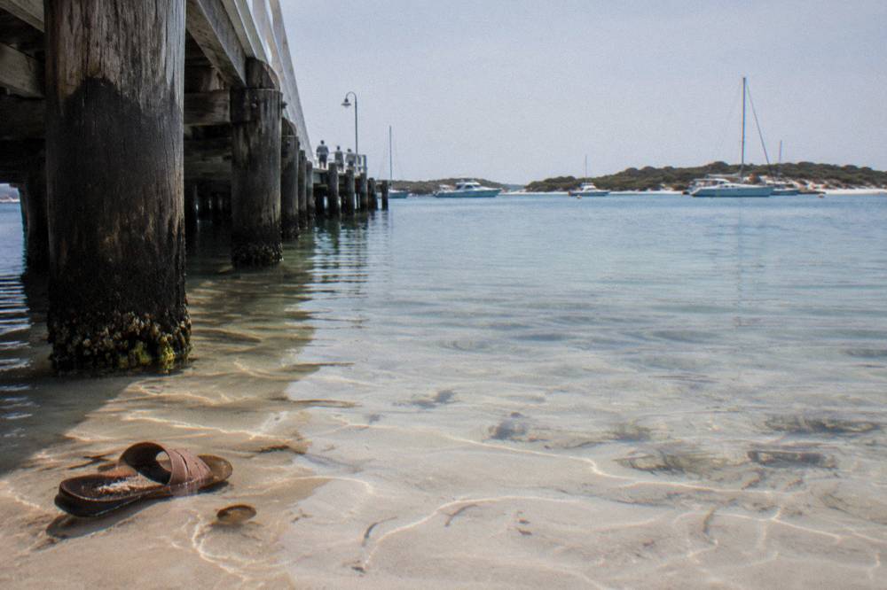 A calm bay with clear shallow water over pale sand and moored boats in the distance
