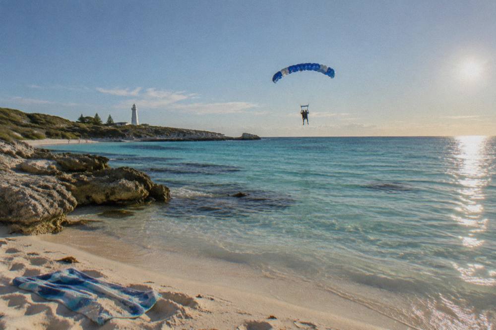 A tandem skydiver under an open parachute above a turquoise bay