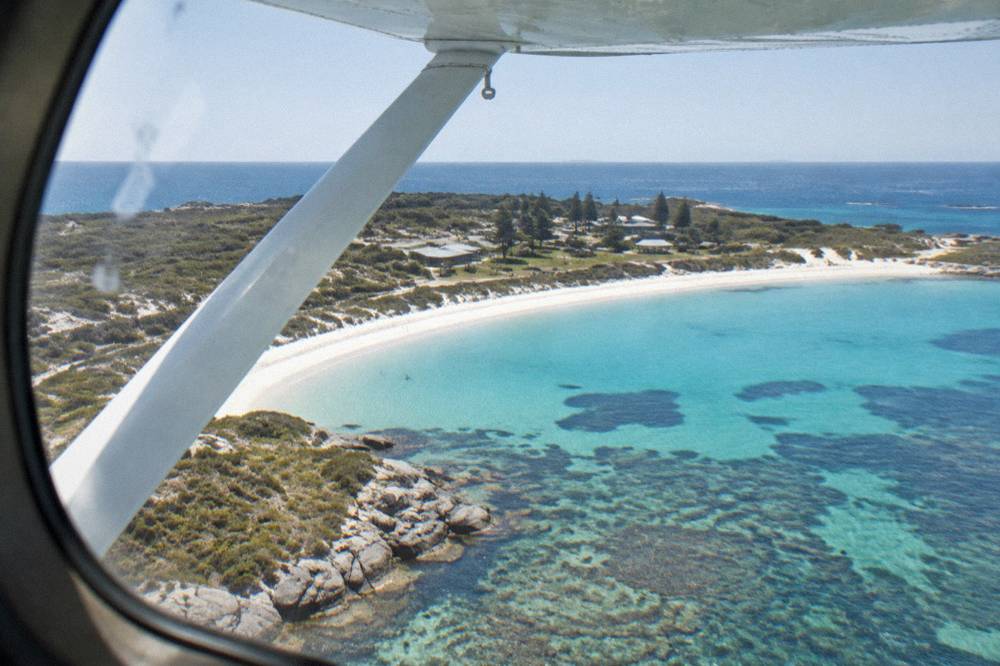 A light aircraft banking over white sand and reef in clear water