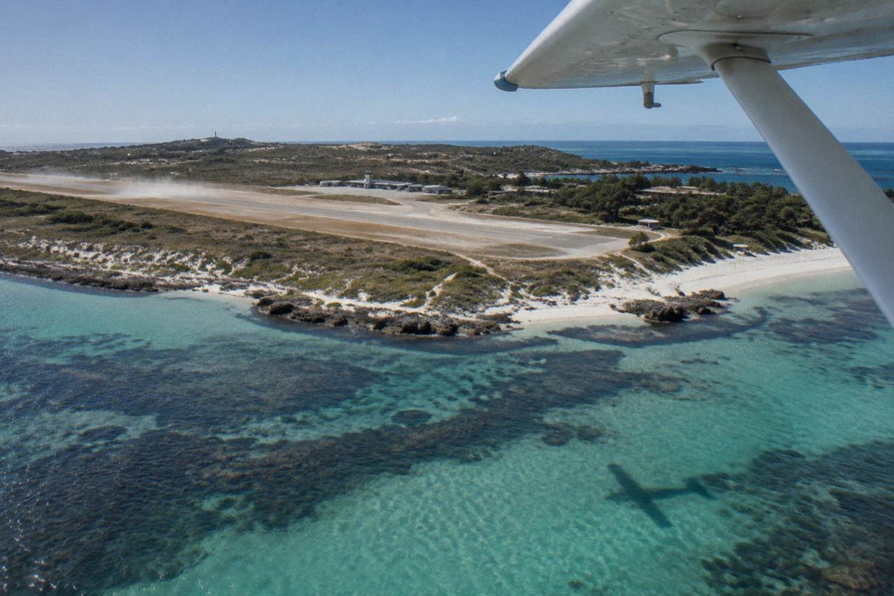A small light aircraft flying over turquoise island bays and white sand